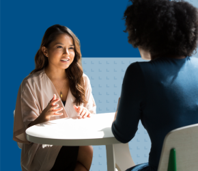 Two people speak to one another across a table.