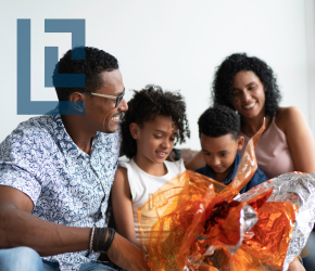 A family smiling together on a grey couch.