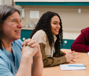 A group of people sit together at a table, listening to a presenter in a writing workshop.