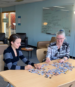 Two people sitting together and doing a puzzel in the Community Commons space. 