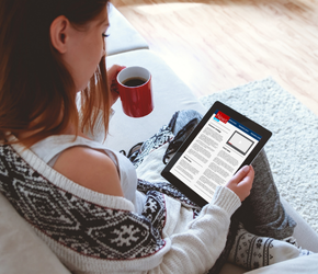 A woman checking her favourite morning paper with a red mug of coffee.