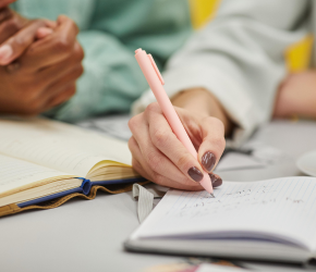 A hand holding pen, writing in a notebook.