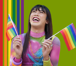 A woman laughing and holding a rainbow pride flag in each hand.