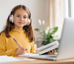 A child with headphones on studies in front of a cumputer