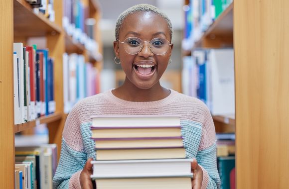 A Black woman in a pink and blue sweater holding a stack of books and smiling