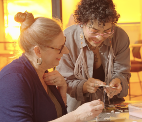 An Indigenous person helping a woman with a beading project