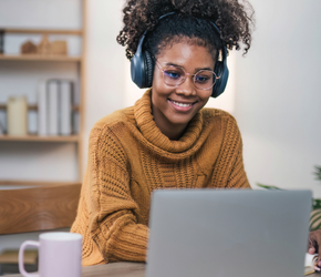 A womanwith headphones on studies in front of a cumputer