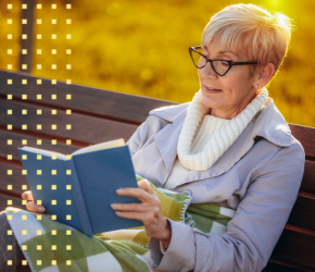 A woman reading a book on a park bench. 