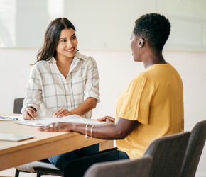 Two people sitting at a table looking over resumes. 